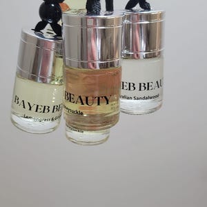 May include: Three small glass bottles with silver lids hang from black cords. The bottles contain scented oils labeled "BAYEB BE" with "Lemongrass & Ginger", "BEAUTY" with "Honeysuckle", and "EB BEAU" with "Australian Sandalwood".