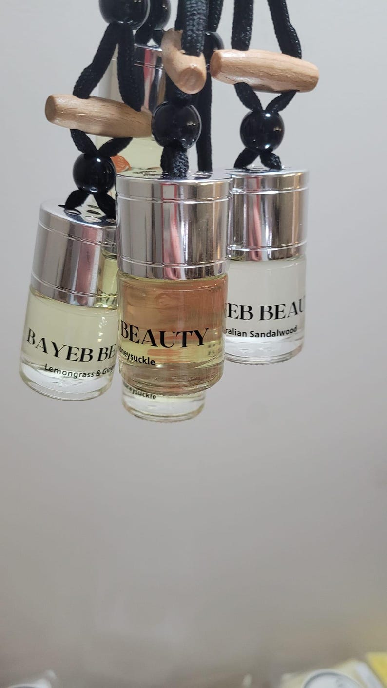 May include: Three small glass bottles with silver lids hang from black cords. The bottles contain scented oils labeled "BAYEB BE" with "Lemongrass & Ginger", "BEAUTY" with "Honeysuckle", and "EB BEAU" with "Australian Sandalwood".