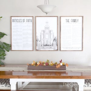 Puede incluir: Tres impresiones enmarcadas en una pared blanca sobre una mesa de comedor de madera. Las impresiones son en blanco y negro y presentan texto y un dibujo de un edificio. La mesa tiene una tapa de madera y patas blancas. Una caja de madera llena de hojas de otoño se encuentra sobre la mesa.