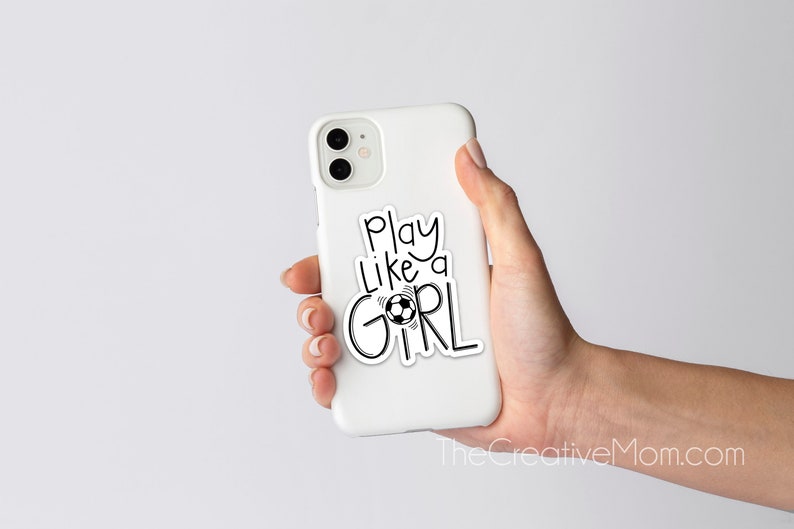 May include: White phone case with a black and white sticker that says "Play like a girl" with a soccer ball graphic.