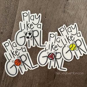 May include: Three white stickers with black text that reads "Play Like a Girl" with a different sports ball on each sticker. The sports balls are a soccer ball, a basketball, and a softball.