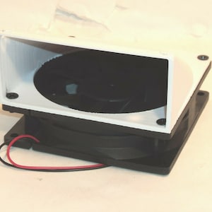May include: A white plastic fan shroud with a black fan and wires attached. The fan is mounted on a black base.