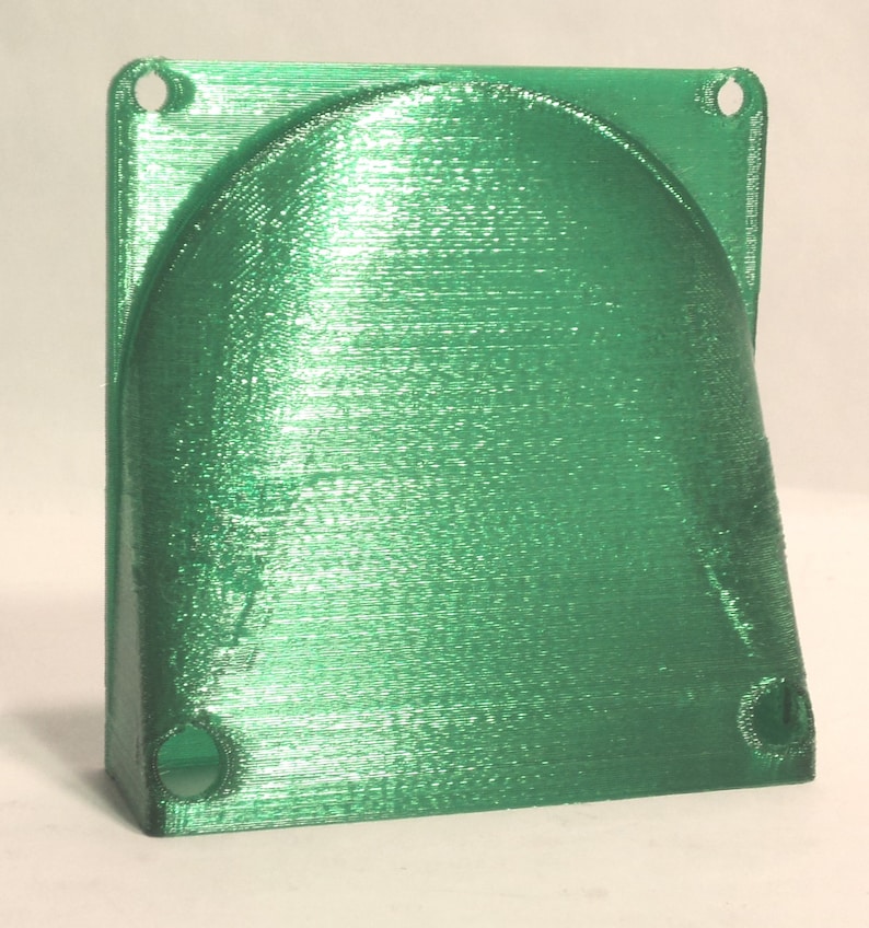 May include: A green plastic 3D printed fan shroud with two holes on the top and two holes on the bottom.