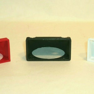 Puede incluir: Tres peque&ntilde;os soportes de exhibici&oacute;n de pl&aacute;stico angulados con un recorte circular. Los soportes son rojo, negro y blanco.
