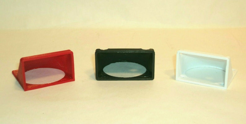 Puede incluir: Tres peque&ntilde;os soportes de exhibici&oacute;n de pl&aacute;stico angulados con un recorte circular. Los soportes son rojo, negro y blanco.