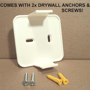 May include: A white, square-shaped wall mount with two support arms and two screw holes. The image includes two silver screws and two yellow drywall anchors. Text at the top reads: COMES WITH 2x DRYWALL ANCHORS & SCREWS!