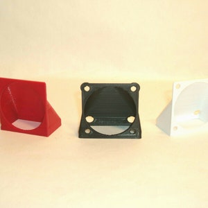 Puede incluir: Tres soportes para ventiladores impresos en 3D en rojo, negro y blanco. Cada soporte tiene una base cuadrada con una abertura circular para un ventilador.