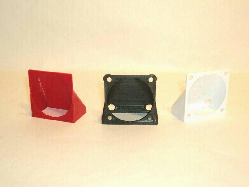 Puede incluir: Tres soportes para ventiladores impresos en 3D en rojo, negro y blanco. Cada soporte tiene una base cuadrada con una abertura circular para un ventilador.