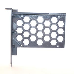 Puede incluir: Una cubierta de ranura de expansión para computadora impresa en 3D de color gris oscuro, con un patrón de panal hexagonal en su superficie rectangular, una placa de montaje perpendicular a la izquierda y cuatro orificios para tornillos.