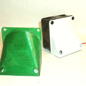 May include: Two 3D-printed components. One is a bright green, curved shape with mounting holes. The other is a black and white rectangular box with a fan and mounting holes. The components are likely for electronics or DIY projects.
