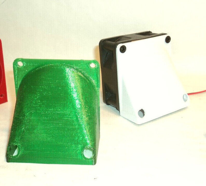 May include: Two 3D-printed components. One is a bright green, curved shape with mounting holes. The other is a black and white rectangular box with a fan and mounting holes. The components are likely for electronics or DIY projects.