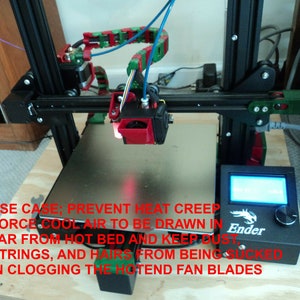 Puede incluir: Una impresora 3D con una gu&iacute;a de filamento roja y verde, una boquilla negra y plateada y un panel de control negro con la palabra "Ender" en &eacute;l. El texto "USE CASE; PREVENT HEAT CREEP FORCE COOL AIR TO BE DRAWN IN FAR FROM HOT BED AND KEEP DUST STRINGS, AND HAIRS FROM BEING SUCKED IN CLOGGING THE HOTEND FAN BLADES" est&aacute; escrito en rojo en la imagen.