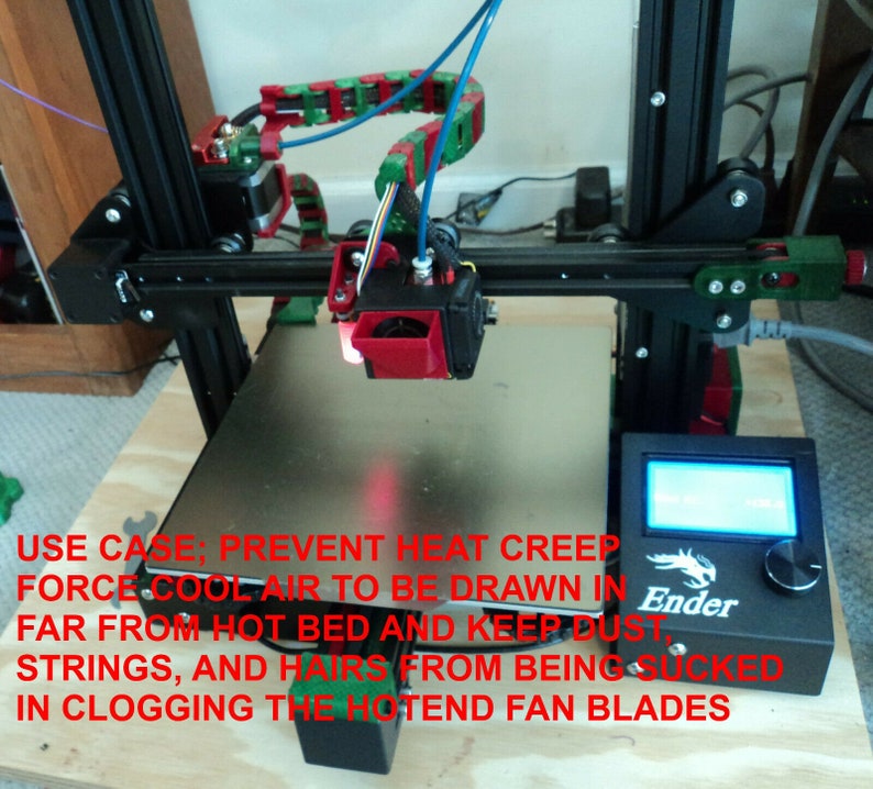 Puede incluir: Una impresora 3D con una gu&iacute;a de filamento roja y verde, una boquilla negra y plateada y un panel de control negro con la palabra "Ender" en &eacute;l. El texto "USE CASE; PREVENT HEAT CREEP FORCE COOL AIR TO BE DRAWN IN FAR FROM HOT BED AND KEEP DUST STRINGS, AND HAIRS FROM BEING SUCKED IN CLOGGING THE HOTEND FAN BLADES" est&aacute; escrito en rojo en la imagen.