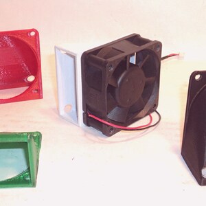 May include: An assortment of 3D-printed components, including a red circular housing, a green rectangular piece, a black fan, and a black angled piece. The fan is black with a central fan blade and red and black wires.