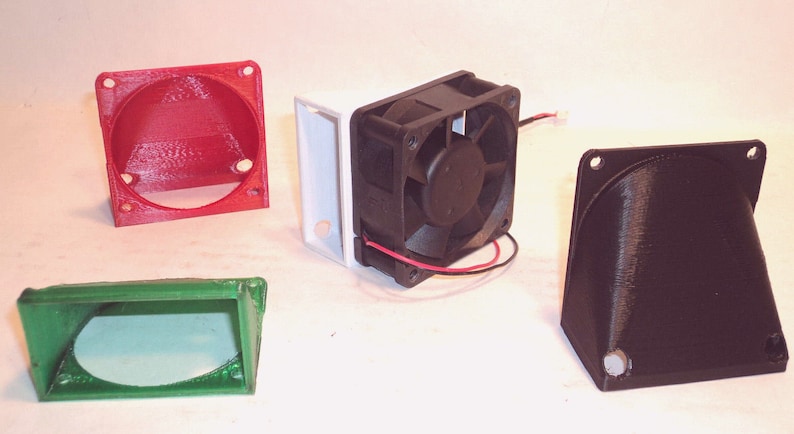 May include: An assortment of 3D-printed components, including a red circular housing, a green rectangular piece, a black fan, and a black angled piece. The fan is black with a central fan blade and red and black wires.