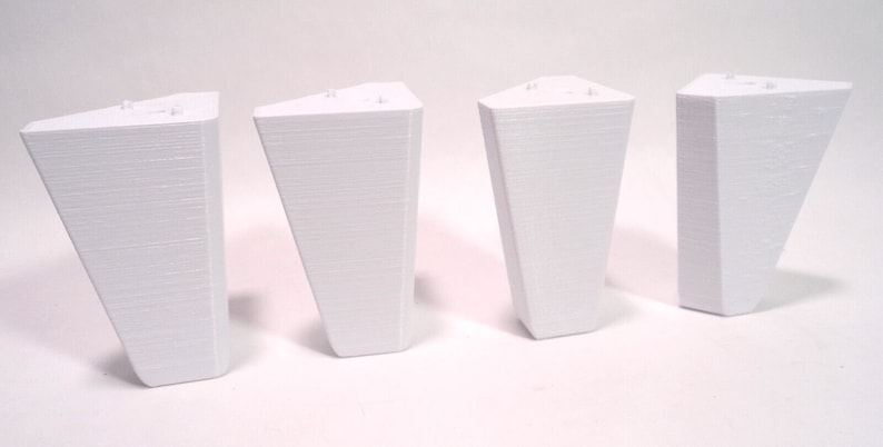 Puede incluir: Cuatro patas de muebles de pl&aacute;stico blanco. Cada pata tiene forma triangular y una superficie lisa ligeramente texturizada.
