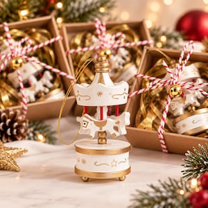 May include: A white and gold carousel ornament featuring a central rotating horse, a conical roof, and a circular base with star and swirl patterns. The ornament includes a thin gold hanging string and is crafted with painted wooden details.