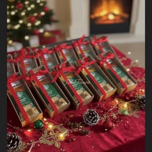 May include: A collection of rectangular cardboard gift boxes, each containing a Starbucks Hazelnut Latte drink mix packet. Every box is tied with a bright red satin ribbon bow. The boxes are arranged in rows on a deep red velvet tablecloth.