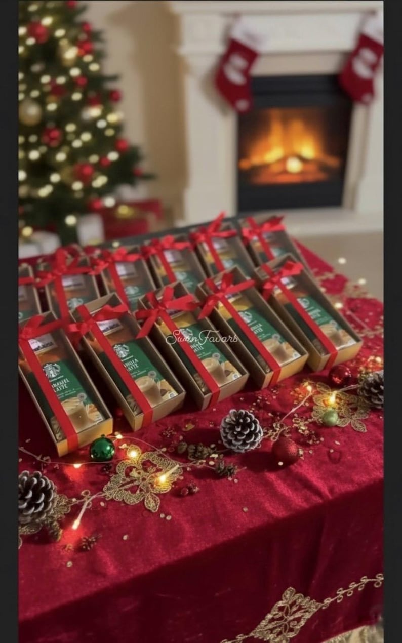 May include: A collection of rectangular cardboard gift boxes, each containing a Starbucks Hazelnut Latte drink mix packet. Every box is tied with a bright red satin ribbon bow. The boxes are arranged in rows on a deep red velvet tablecloth.