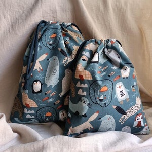 May include: Two blue drawstring bags with a white background and a pattern of various animals, including penguins, seals, foxes, and owls. The bags are made of fabric and have a drawstring closure.