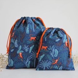 May include: Two drawstring bags with a blue background and orange drawstrings. The bags feature a repeating pattern of monkeys, palm trees, and leaves.