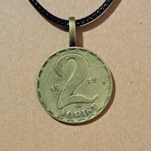 May include: A gold-colored 2 Forint coin pendant on a black cord necklace. The coin has the number "2" and the year "1975" inscribed on it.