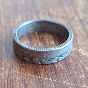 Könnte beinhalten: Ein silberner Ring aus einer japanischen Münze. Der Ring hat ein detailliertes Design mit japanischen Schriftzeichen und Symbolen.
