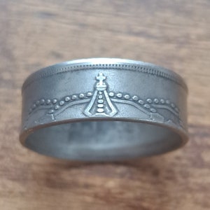 Könnte beinhalten: Ein silberner Ring aus einer wiederverwendeten Münze. Der Ring zeigt ein detailliertes Design mit einem Kreuz und einer Krone.