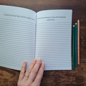 Puede incluir: Un cuaderno abierto con p&aacute;ginas rayadas. La p&aacute;gina izquierda tiene el texto "A quirk you have that I think is really cute..." y la p&aacute;gina derecha tiene el texto "My favorite memory of you from the past week was..." Tres l&aacute;pices de colores est&aacute;n en el lado derecho del cuaderno.