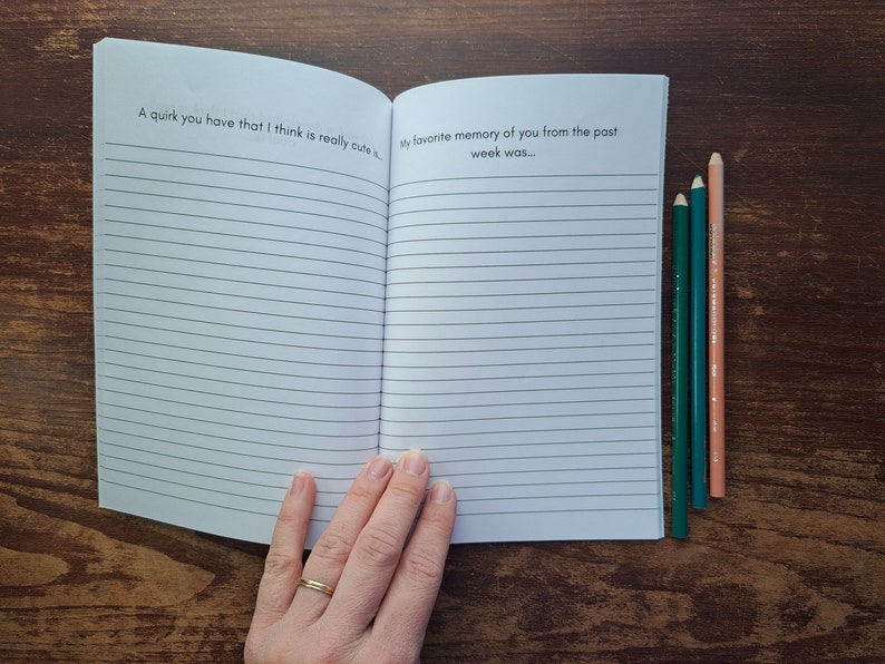 Puede incluir: Un cuaderno abierto con p&aacute;ginas rayadas. La p&aacute;gina izquierda tiene el texto "A quirk you have that I think is really cute..." y la p&aacute;gina derecha tiene el texto "My favorite memory of you from the past week was..." Tres l&aacute;pices de colores est&aacute;n en el lado derecho del cuaderno.