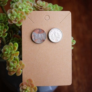 May include: Two silver British five pence coins on a brown card with a hole in the top. The coins are slightly worn and have a copper patina.