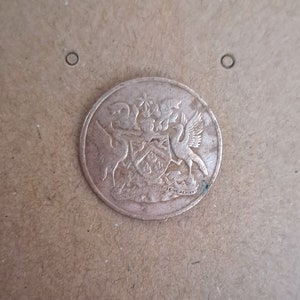 May include: A close-up of a copper-colored coin with a design featuring two birds and a shield. The text "THE WEALTH" is visible on the bottom of the coin.