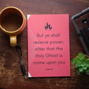 Könnte beinhalten: Ein rechteckiger roter Druck mit einem schwarzen Flammensymbol und dem Text: But ye shall receive power, after that the Holy Ghost is come upon you. Acts 1:8. Der Druck liegt neben einer gelben Tasse, einem schwarzen Stift, einer Schreibmaschine und einer kleinen Sukkulente.
