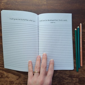 Puede incluir: Un cuaderno abierto con p&aacute;ginas rayadas. La p&aacute;gina izquierda tiene el texto "It still gives me butterflies when you..." y la p&aacute;gina derecha tiene el texto "A skill you've developed that I think is really cool is..."