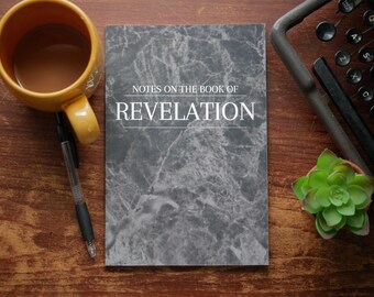 May include: A notebook with a grey marble pattern cover featuring the white text "NOTES ON THE BOOK OF REVELATION" centred on the front. The notebook is positioned alongside a yellow mug, a black pen, a typewriter, and a small green succulent.