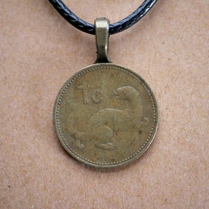 Puede incluir: Un collar con un colgante redondo de color dorado. El colgante es una moneda redonda con el número "1c" y una imagen estilizada de un animal.