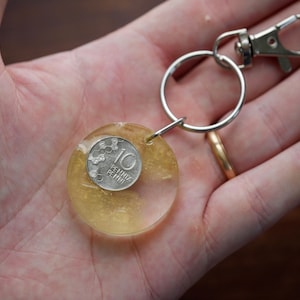 May include: A clear, round keychain with a silver coin embedded in a yellow resin. The coin has the number 10 and text. The keychain has a silver ring and a metal clasp.