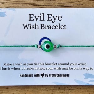 May include: Green string bracelet with a blue and green evil eye charm. The bracelet is tied around a white card with the text "Evil Eye Wish Bracelet". The card also includes the text "Make a wish as you tie this bracelet around your wrist. And has it when it breaks in two, your wish may be on its way to. Handmade with By PrettyCharmsGB".
