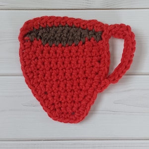 May include: A crocheted red coffee cup coaster with a brown crocheted rim. The coaster is shaped like a coffee cup with a handle.