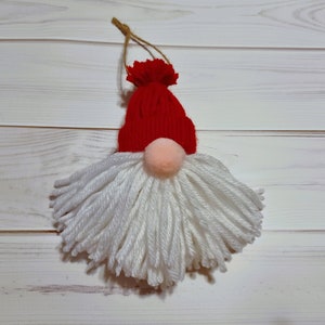 May include: A white yarn gnome ornament with a red knit hat and a white pom-pom nose.