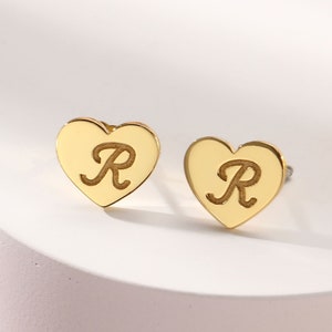May include: A pair of gold heart-shaped earrings with the letter "R" engraved on each.