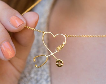 May include: Gold necklace with a heart-shaped pendant that says "Olive" and a stethoscope design.