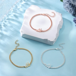 May include: Three bracelets with a chain design. One is rose gold, one is gold, and one is silver. Each bracelet has a pendant with Arabic script. The bracelets are displayed on a white block against a blue background.