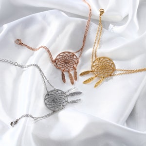 May include: Three gold-toned dreamcatcher bracelets with delicate feather charms. The bracelets are layered on a white fabric background.