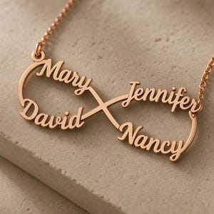 Può includere: Una collana in metallo color oro rosa con un ciondolo a forma di simbolo dell'infinito. Il ciondolo è integrato nella catenina e presenta quattro nomi scritti in corsivo: Mary, David, Jennifer e Nancy, che formano gli anelli del simbolo.