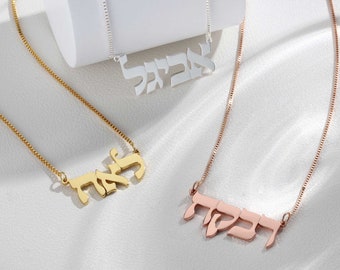 May include: Three gold necklaces with Hebrew lettering pendants. The necklaces are on a white surface.