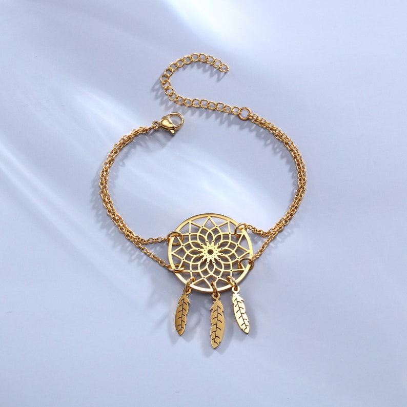 May include: A gold-tone bracelet with a dreamcatcher charm featuring a delicate, intricate design and three dangling feathers.