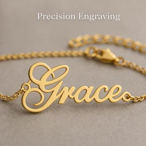 Peut inclure: Un bracelet en métal doré avec une plaque portant le prénom Grace écrit en lettres cursives. Le bracelet est composé d'une fine chaîne avec un fermoir mousqueton. Le texte Precision Engraving est visible en haut de l'image.