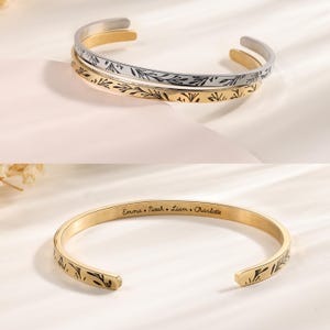 May include: Two gold bangle bracelets with a delicate floral design. The top bracelet is silver and the bottom bracelet is gold. The bottom bracelet is engraved with the names "Emma, Noah, Liam, Charlotte".