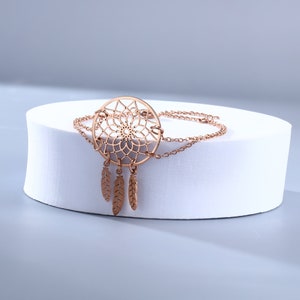 May include: A rose gold dreamcatcher bracelet with a delicate chain and three feather charms.